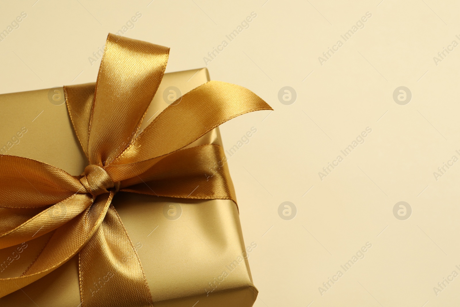 Photo of Beautiful golden gift box on beige background, closeup. Space for text