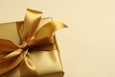 Beautiful golden gift box on beige background, closeup. Space for text