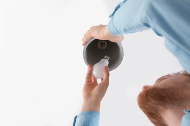 Man changing light bulb in pendant lamp on white background, low angle view