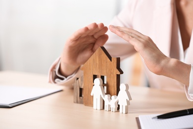 Photo of Female agent covering wooden houses and family at table, closeup. Home insurance
