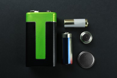 Different types of batteries on black background, flat lay