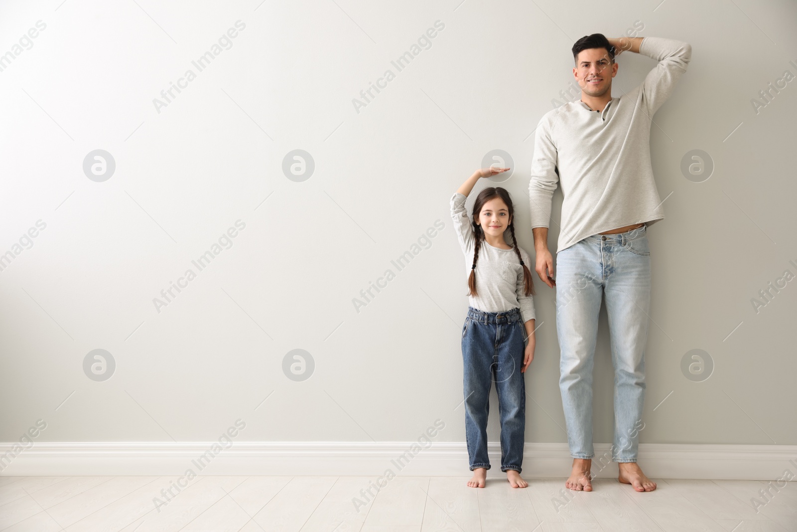 Photo of Little girl and father measuring their height near light grey wall indoors. Space for text