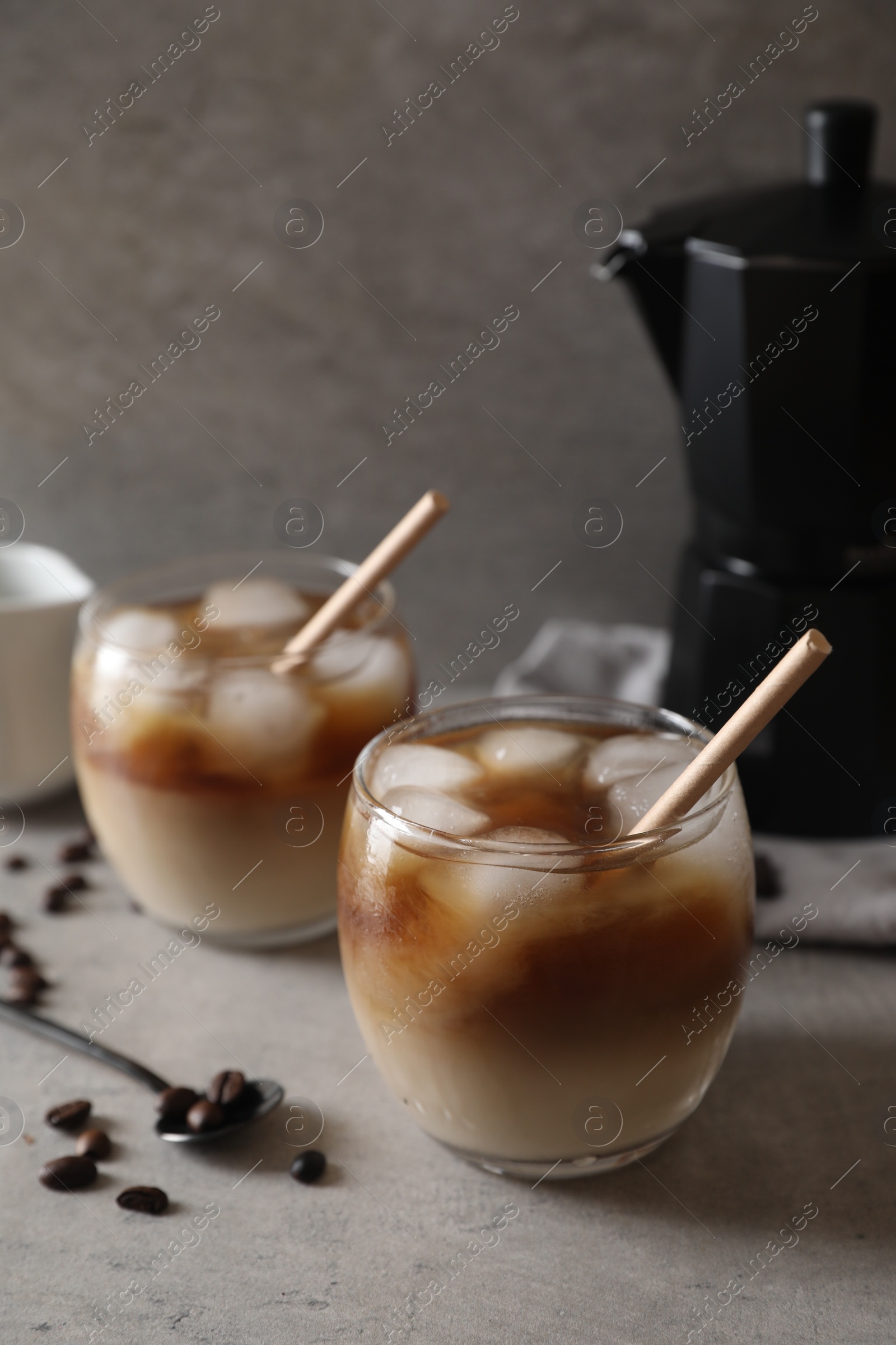 Photo of Refreshing iced coffee with milk in glasses, beans and spoon on gray table, closeup