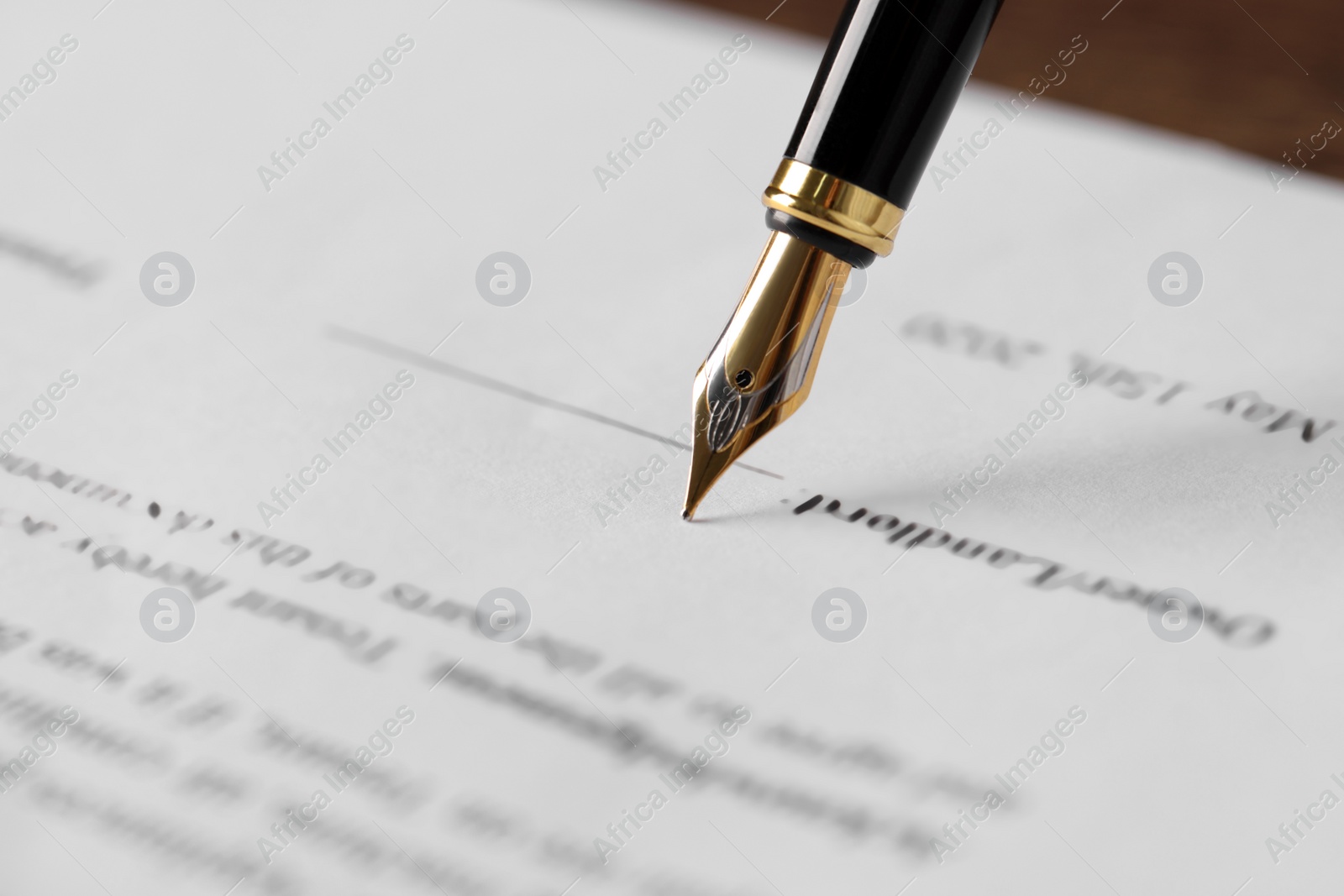 Photo of Writing on document with fountain pen at wooden table, closeup. Notary contract