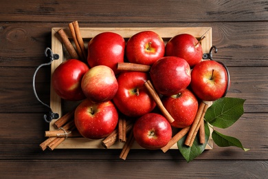 Photo of Fresh apples and cinnamon sticks on wooden table, top view