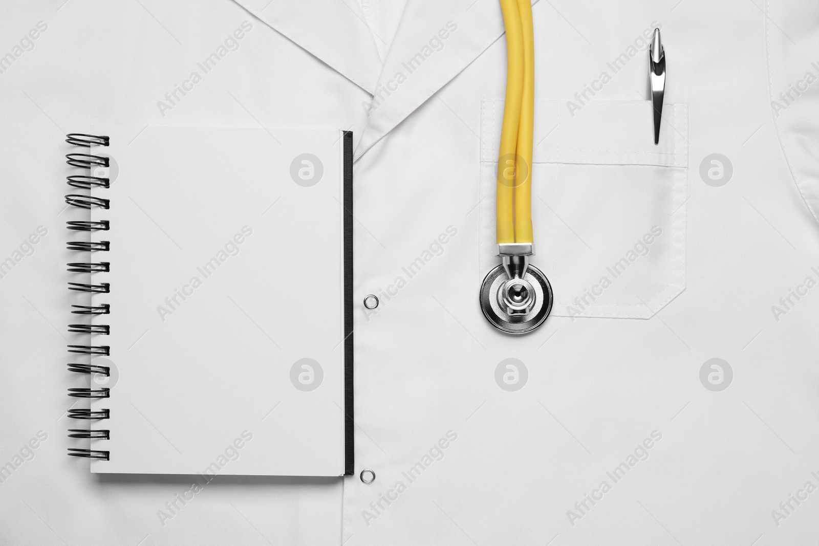 Photo of Stethoscope and notepad on white medical uniform, top view