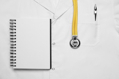 Stethoscope and notepad on white medical uniform, top view