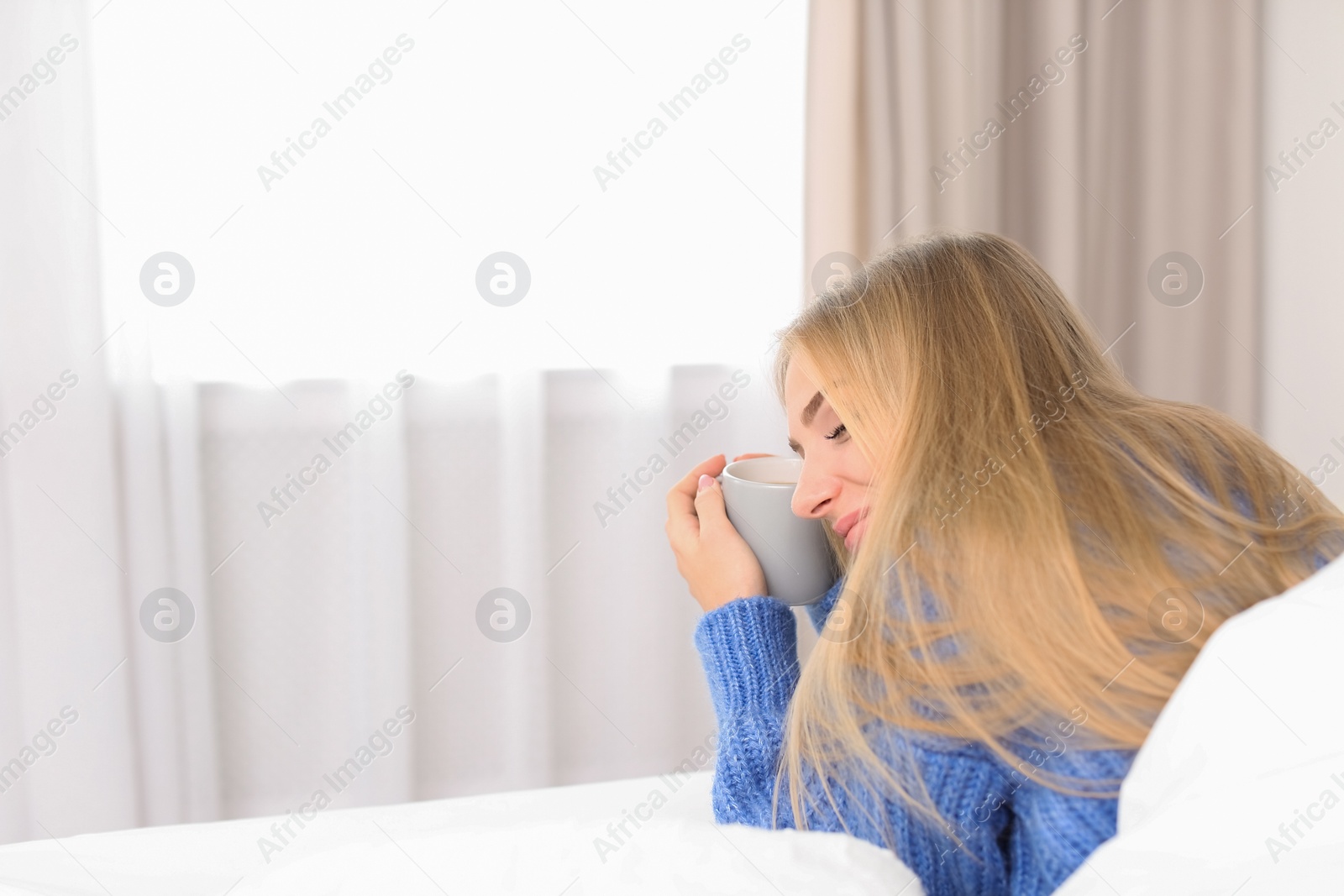 Photo of Beautiful young woman lying with cup in bed at home. Winter atmosphere