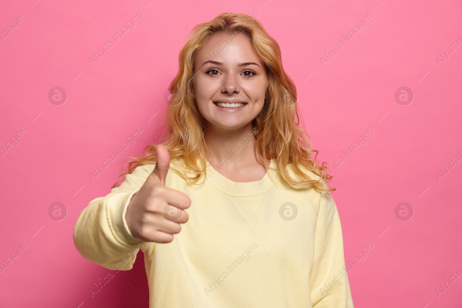 Photo of Happy young woman showing thumb up gesture on pink background