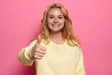 Happy young woman showing thumb up gesture on pink background