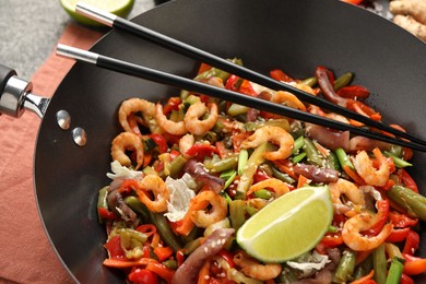 Photo of Shrimp stir fry with vegetables and chopsticks in wok on grey table, closeup