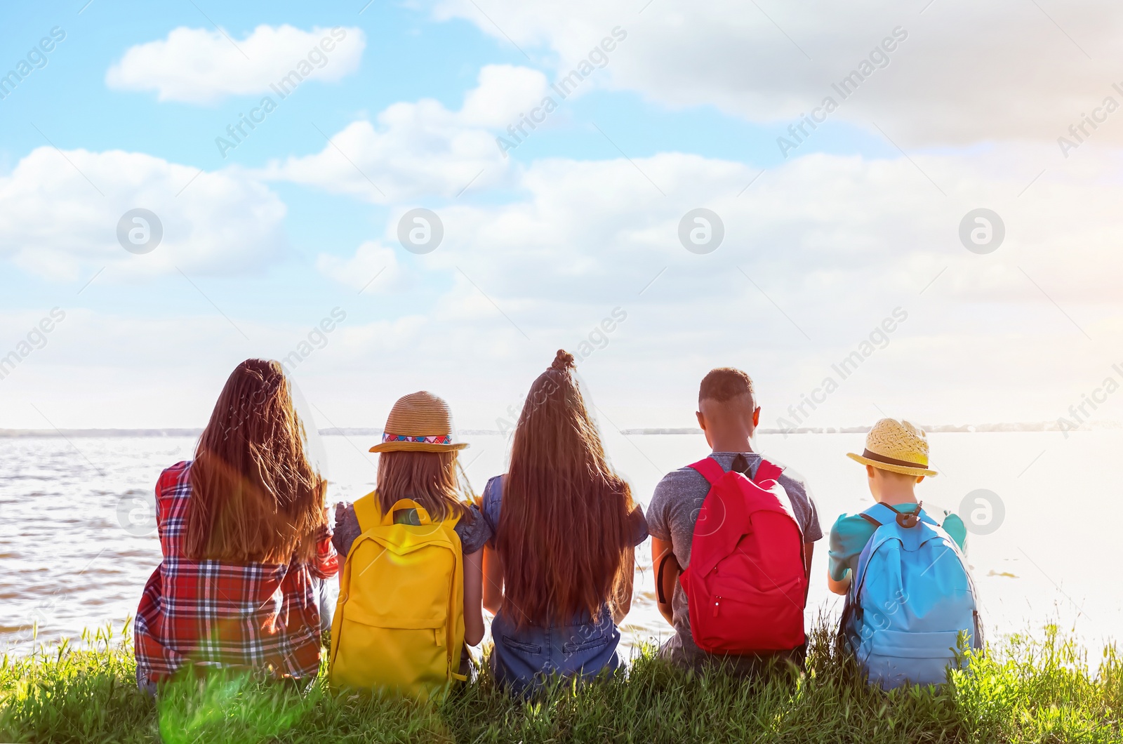 Image of School holidays. Group of children sitting on green grass near river 