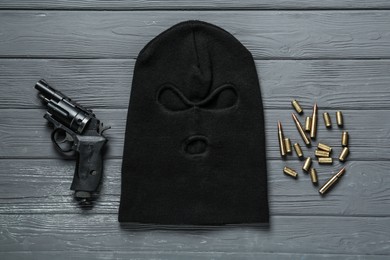 Photo of Balaclava, pistol and bullets on grey wooden table, flat lay