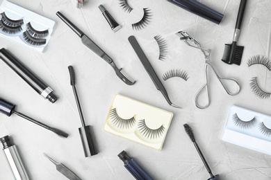 Flat lay composition with false eyelashes, cosmetic products and tools on grey background