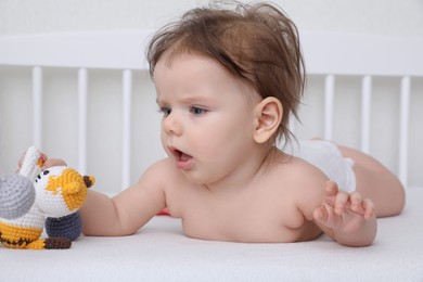 Photo of Cute little baby with toy in comfortable crib at home