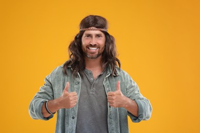 Photo of Stylish hippie man showing thumbs up on orange background