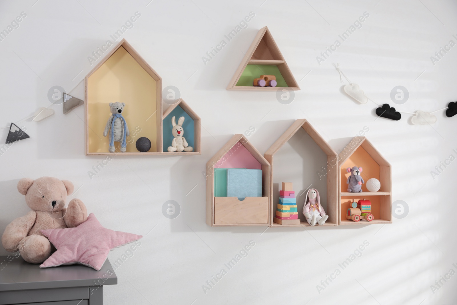 Photo of Cute house shaped shelves and garlands on white wall indoors. Children's room interior design