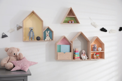 Photo of Cute house shaped shelves and garlands on white wall indoors. Children's room interior design