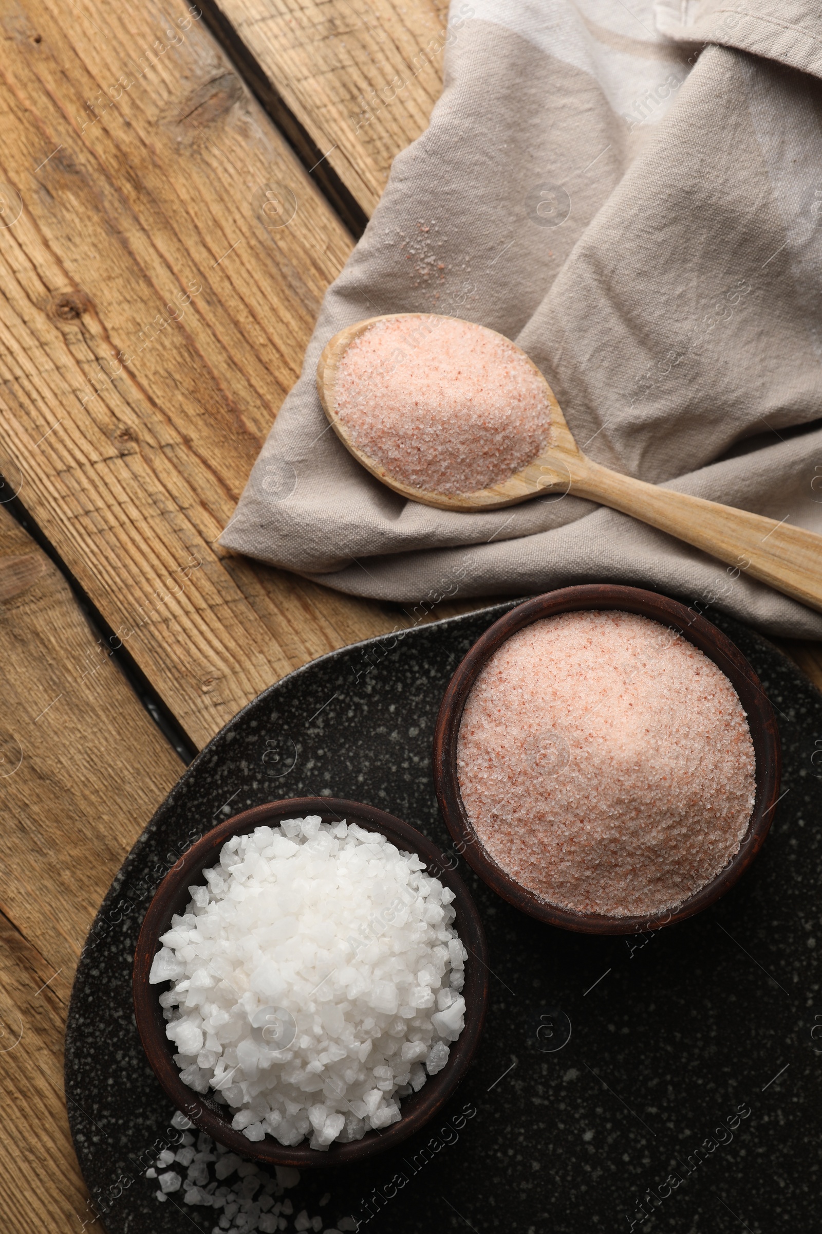 Photo of Different natural salt on wooden table, flat lay