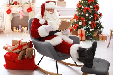 Authentic Santa Claus with glass of milk reading book indoors