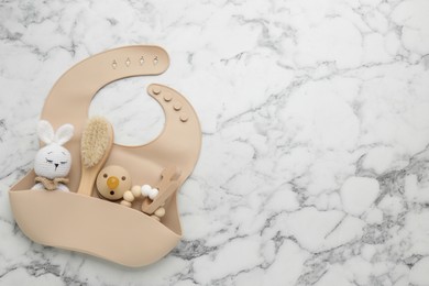 Flat lay composition with silicone baby bib, toys and accessories on white marble background. Space for text