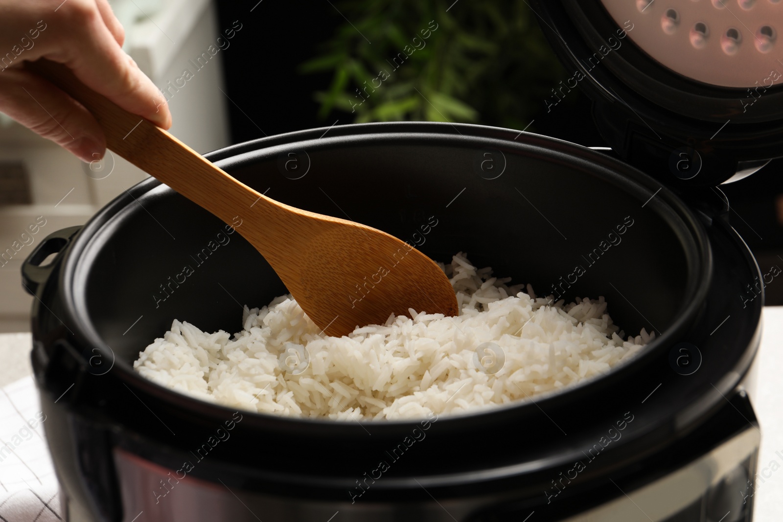 Photo of Woman taking tasty rice with spoon from cooker in kitchen, closeup
