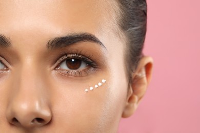 Photo of Woman with cream around eye on pink background, closeup. Skin care