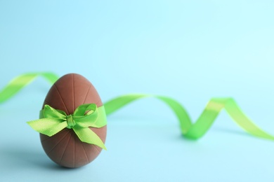 Sweet chocolate egg with bow and ribbon on light blue background. Space for text