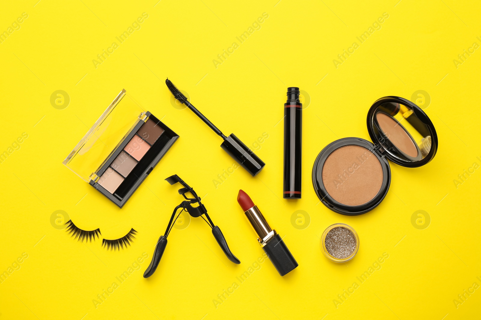 Photo of Eyelash curler and makeup products on yellow background, flat lay