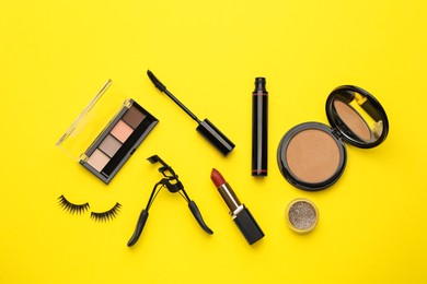 Eyelash curler and makeup products on yellow background, flat lay