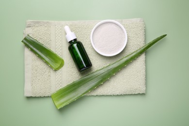 Cosmetic products, aloe leaves and towel on pale green background, top view