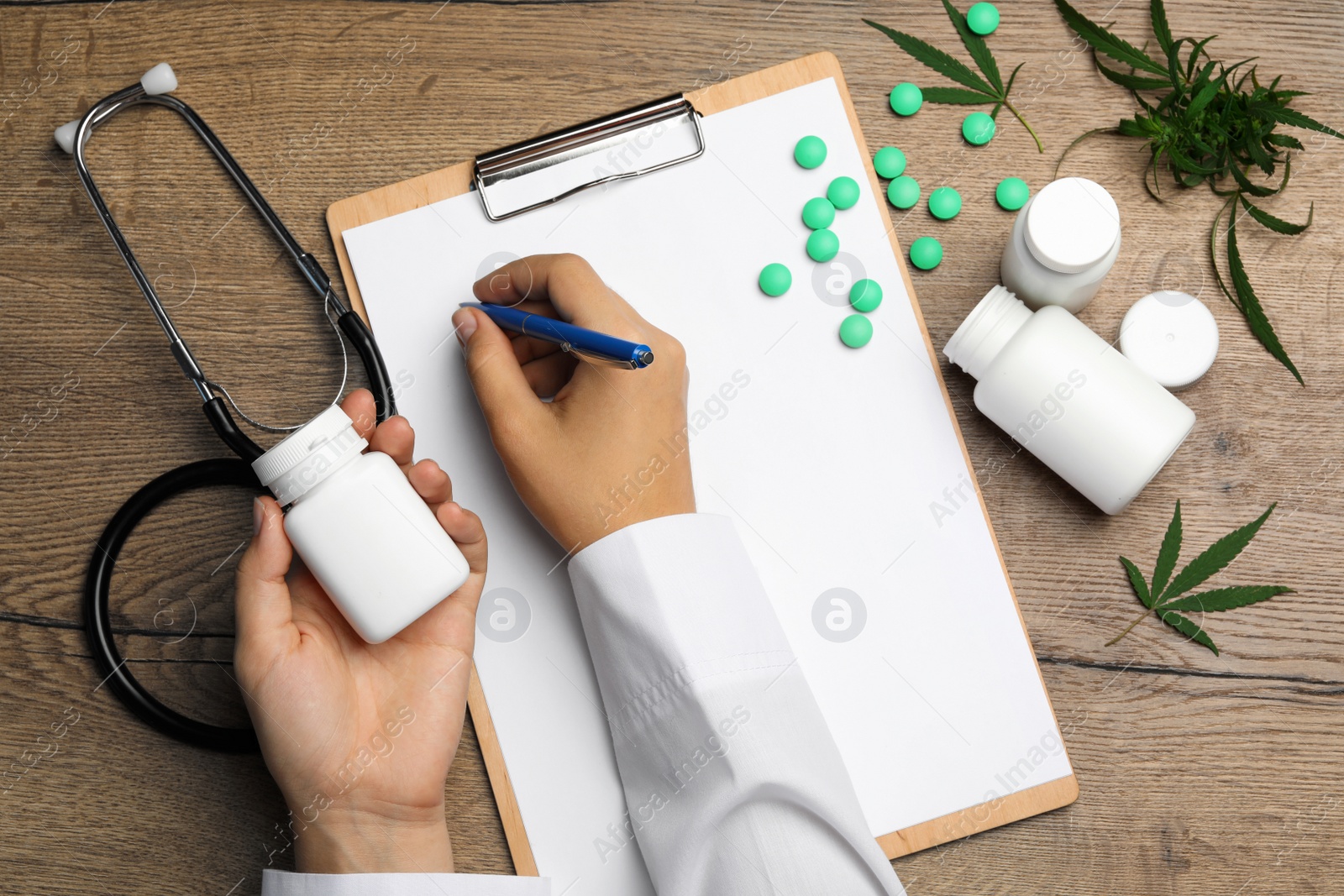 Photo of Female doctor with clipboard, pills and hemp leaves at wooden table, flat lay