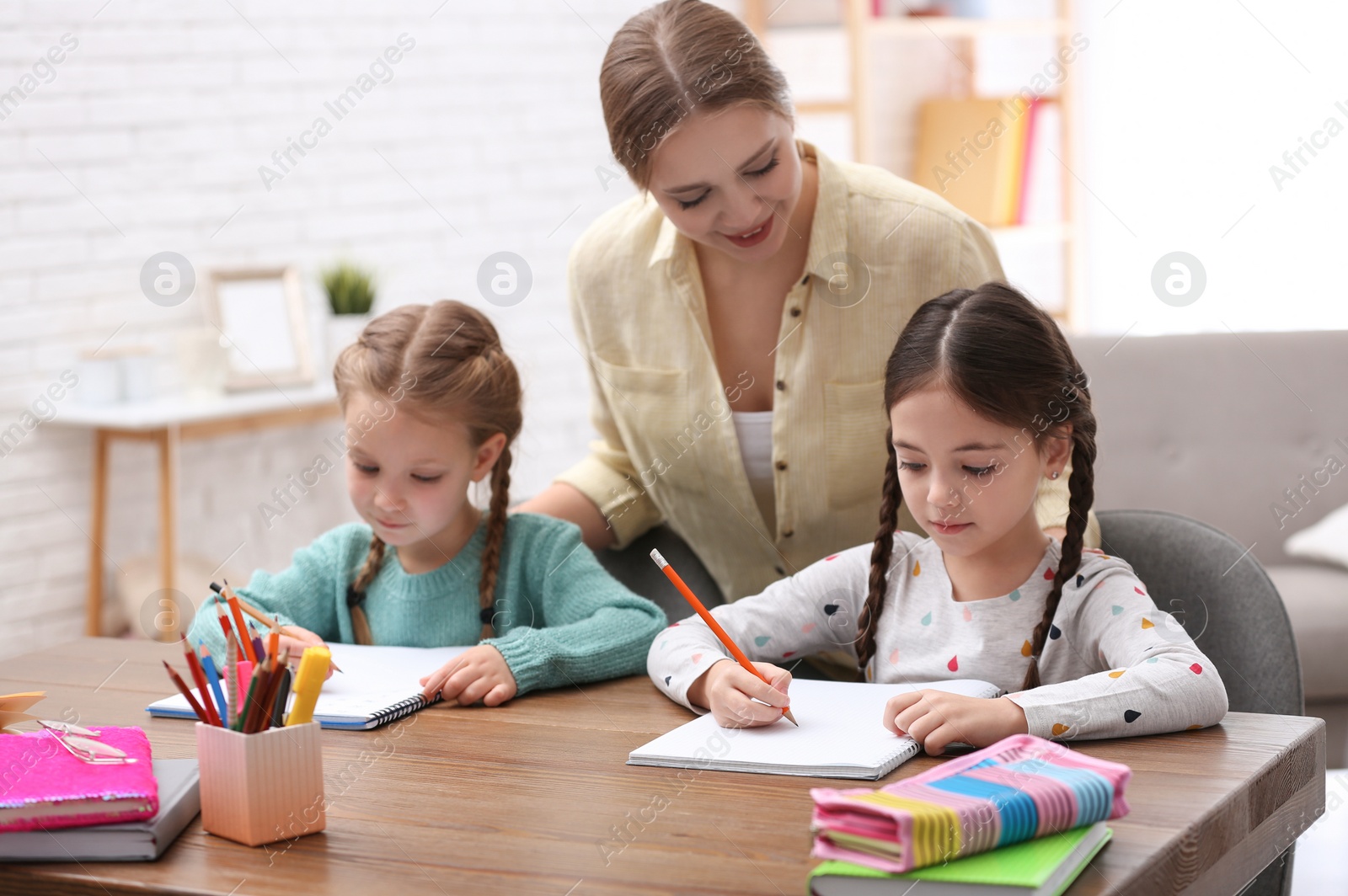 Photo of Mother helping her daughters with homework at table indoors