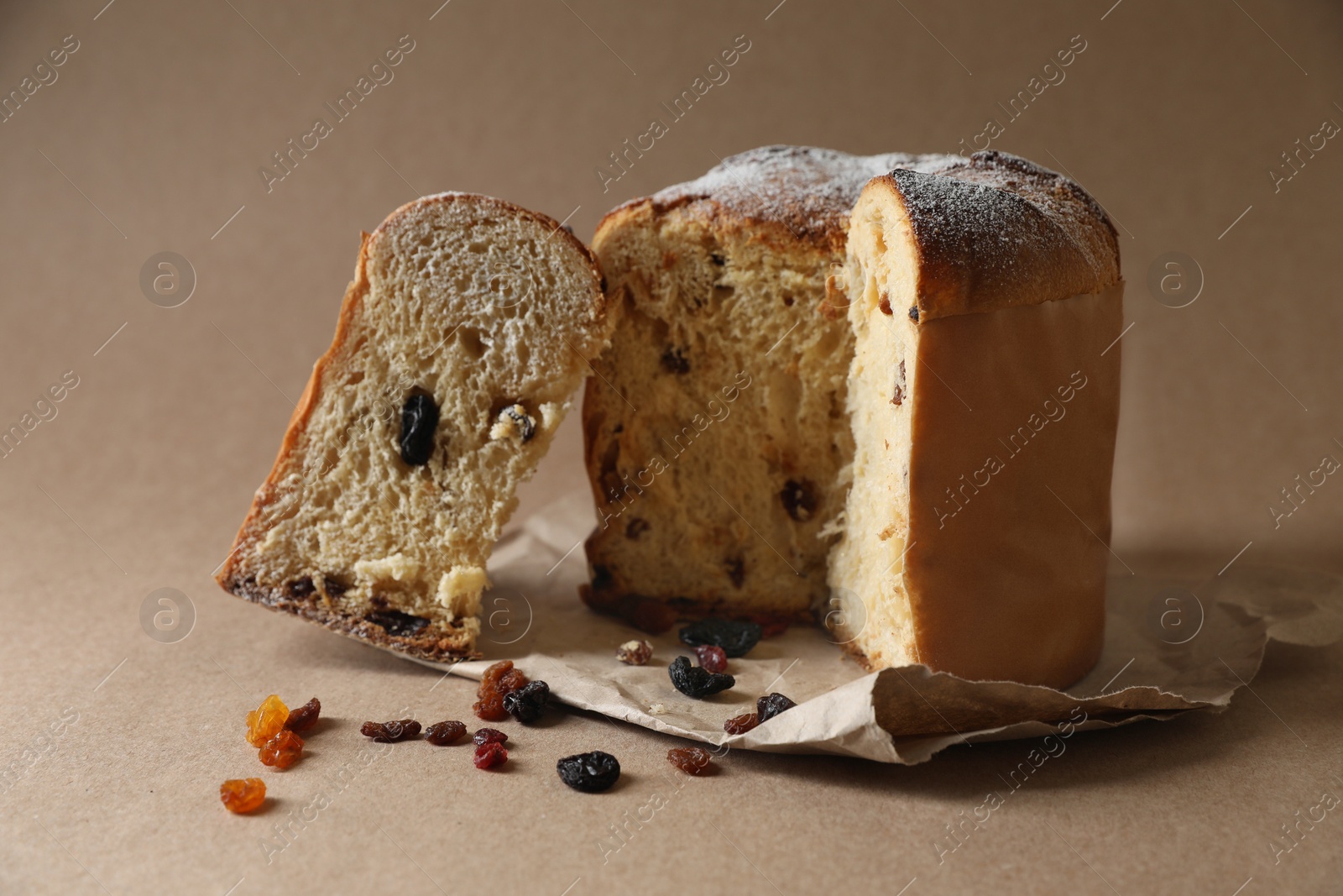 Photo of Delicious cut Panettone cake and raisins on light brown background. Traditional Italian pastry