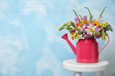 Photo of Watering can with beautiful wild flowers on table against color background