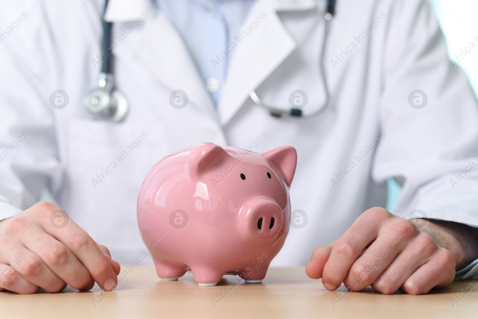 Photo of Doctor with piggy bank at wooden table, closeup