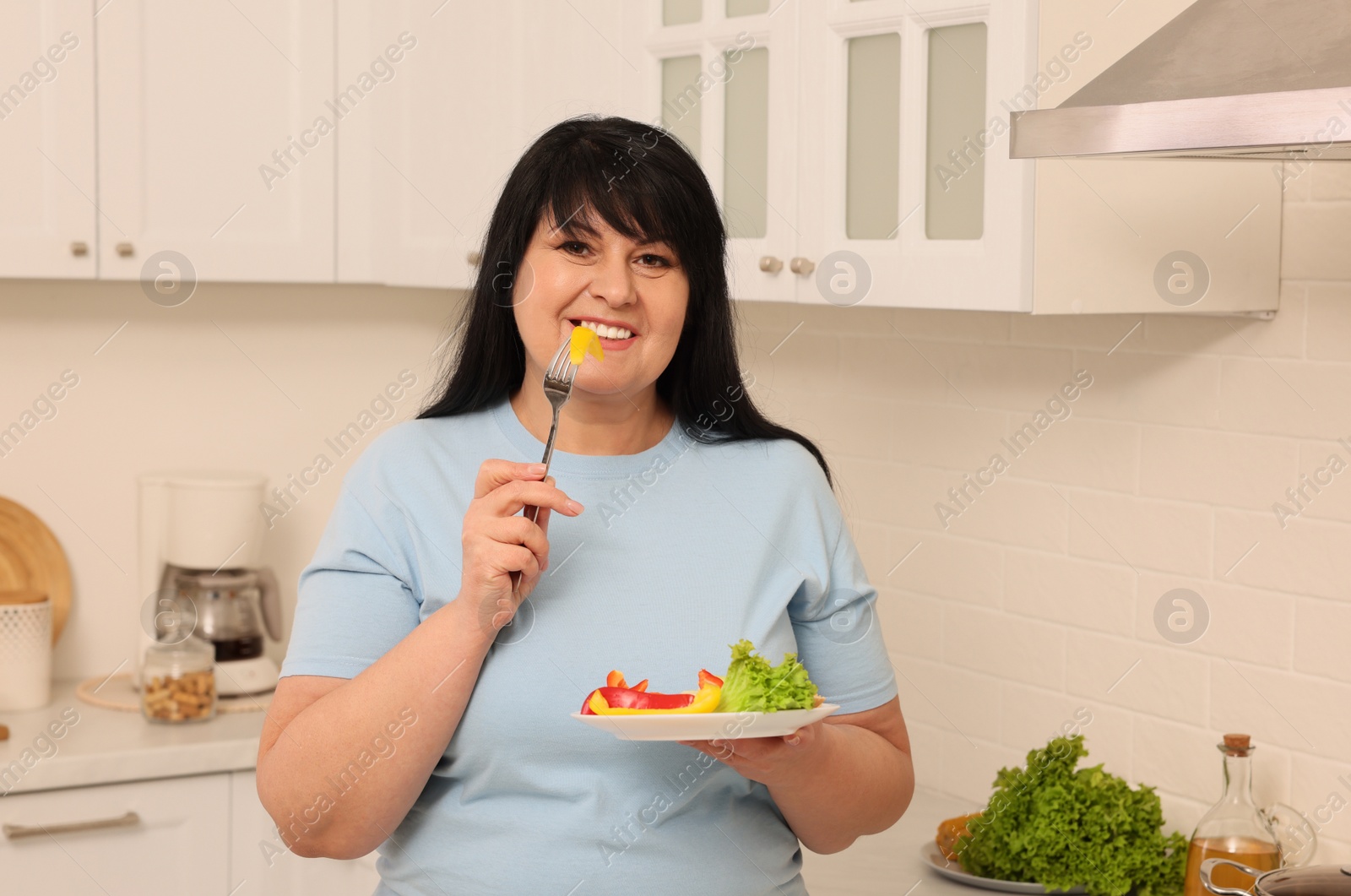 Photo of Happy overweight woman eating salad in kitchen. Healthy diet