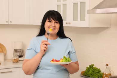 Happy overweight woman eating salad in kitchen. Healthy diet