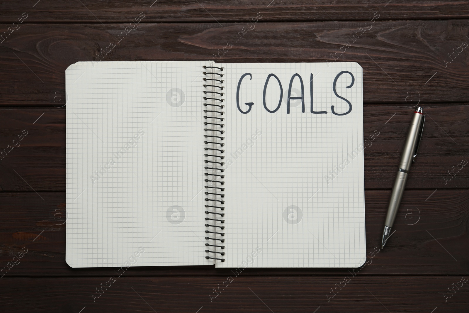 Photo of Notebook with goal list and pen on wooden table, flat lay