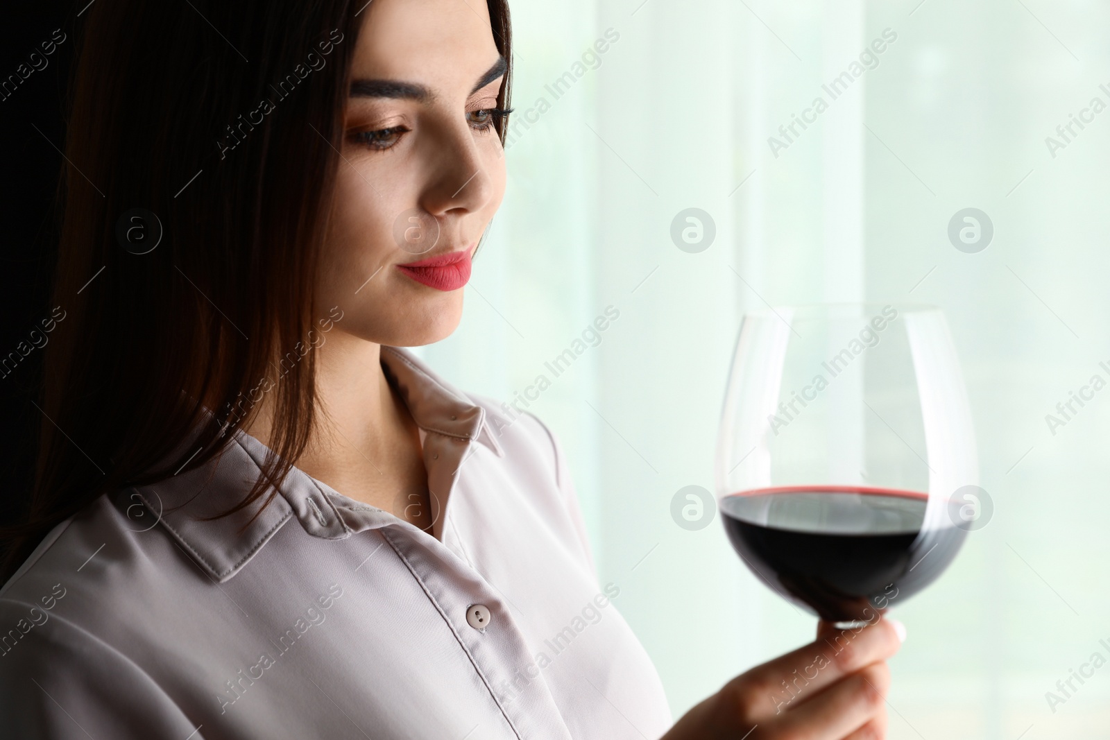 Photo of Beautiful young woman with glass of luxury red wine indoors. Space for text