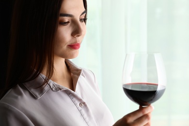 Beautiful young woman with glass of luxury red wine indoors. Space for text