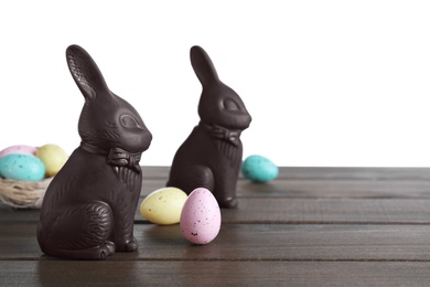 Photo of Dark chocolate Easter bunnies and eggs on wooden table against white background. Space for text