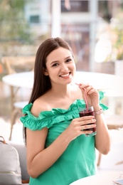 Photo of Young woman with glass of tasty healthy smoothie at table, indoors