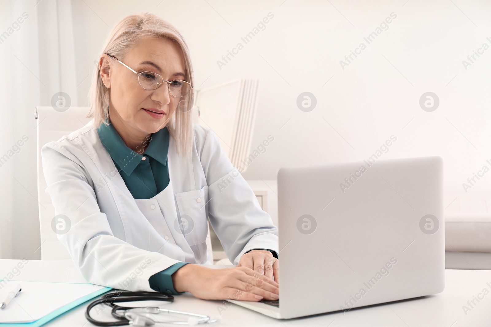 Photo of Mature female doctor working with laptop at table in office