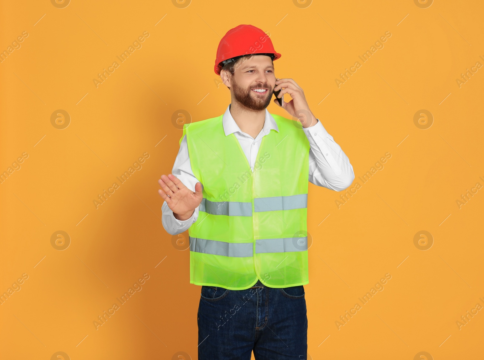 Photo of Man in reflective uniform talking on smartphone against orange background