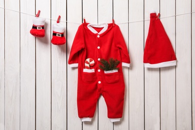 Cute Christmas baby clothes hanging on white wooden wall