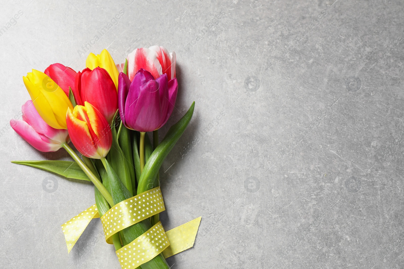 Photo of Beautiful spring tulips on light grey stone table, top view. Space for text