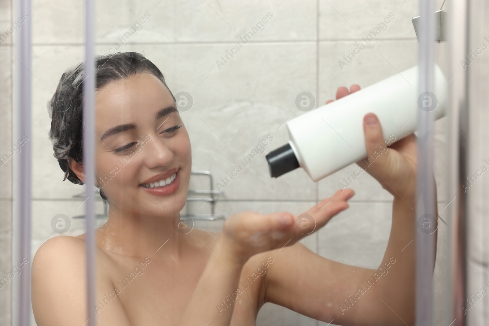 Photo of Happy woman washing hair with shampoo in shower stall, view through glass