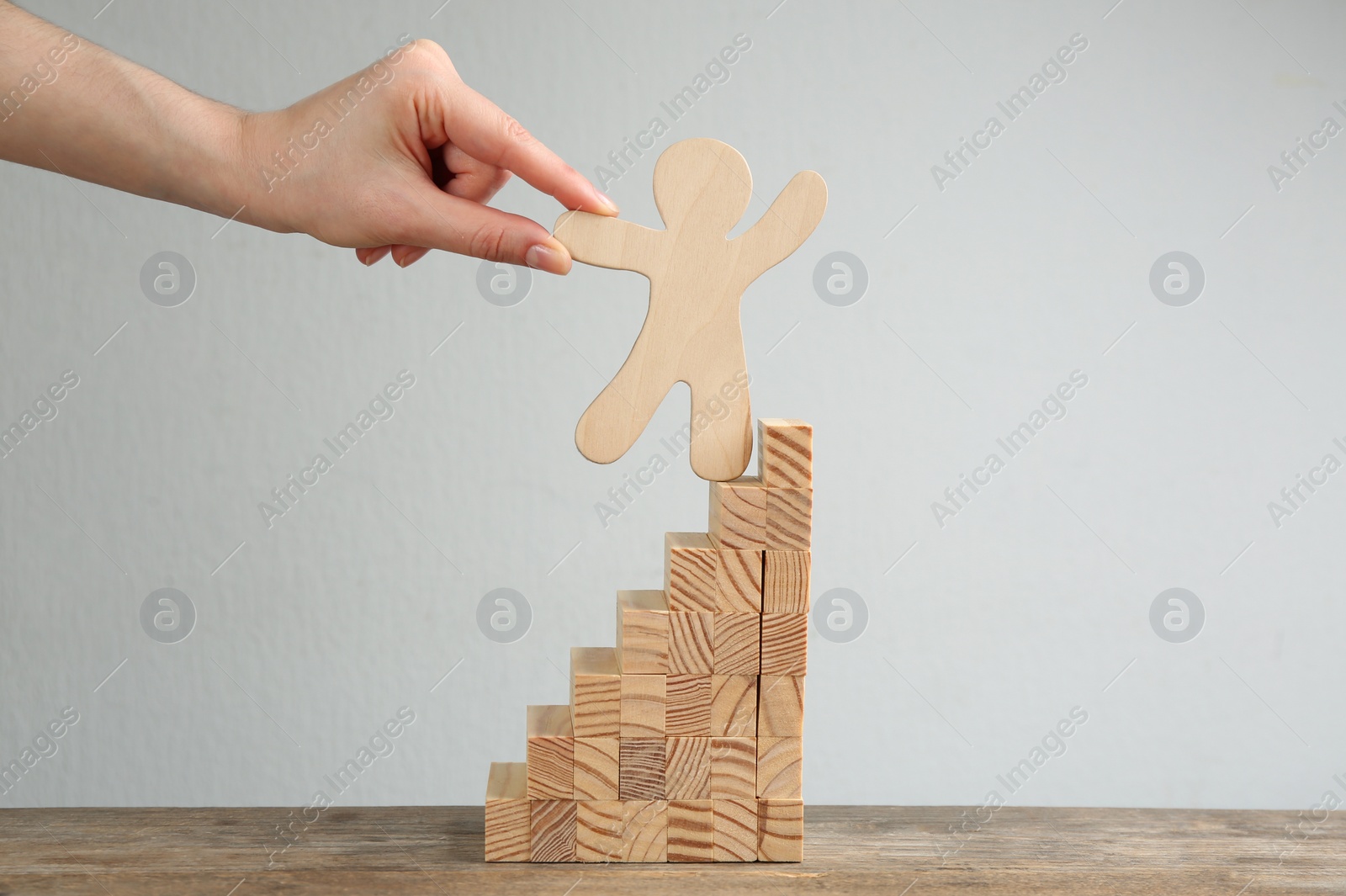 Photo of Closeup view of woman holding human figure on stairs at table. Career promotion concept