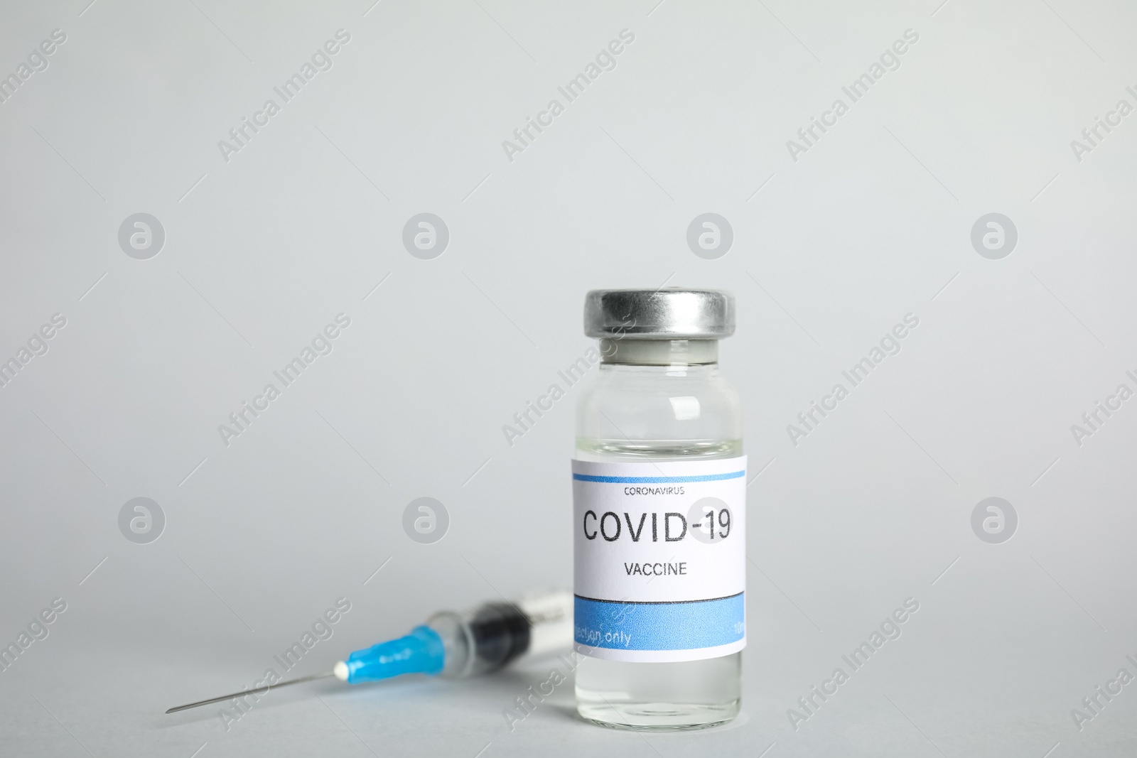 Photo of Vial with coronavirus vaccine and syringe on light background